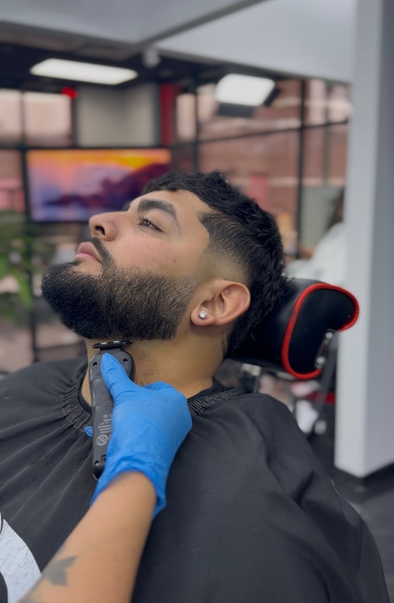 Man with dark beard getting grooming or facial treatment from a barber wearing blue gloves in a modern salon setting