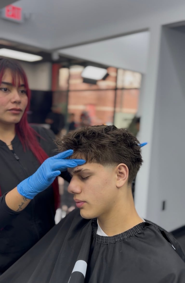 Barber with red hair wearing blue gloves cuts hair of young male client in salon