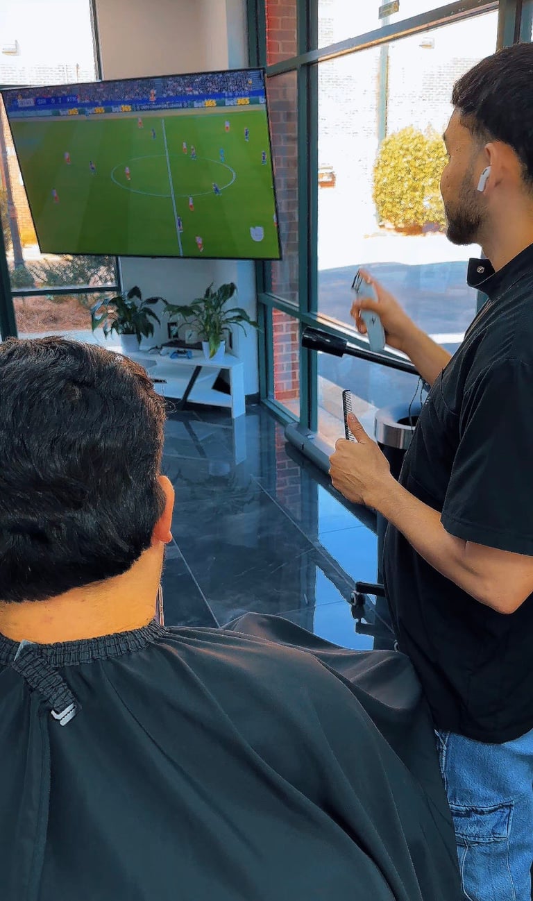 Two men watching a soccer match on a wall-mounted TV in an indoor venue with brick walls and windows