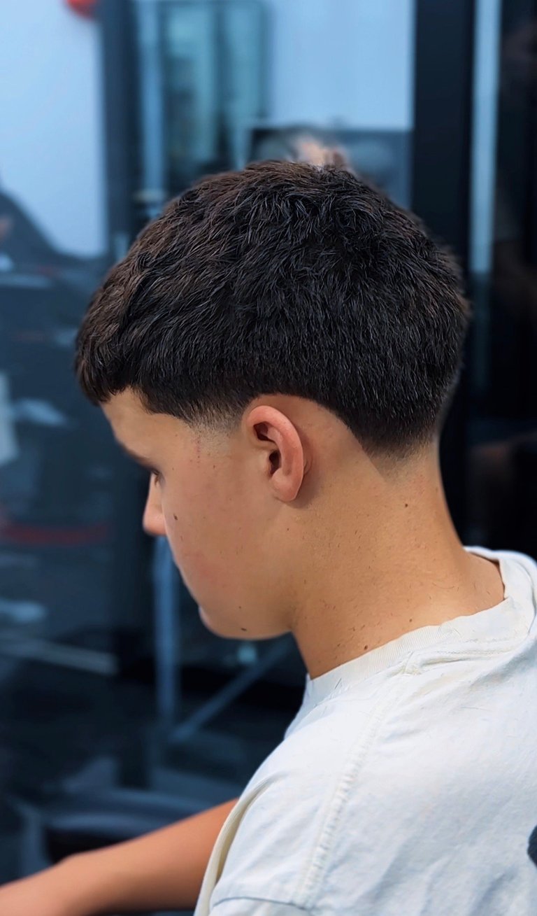 Side profile of a person with short dark hair wearing a white t-shirt, showing a modern fade haircut