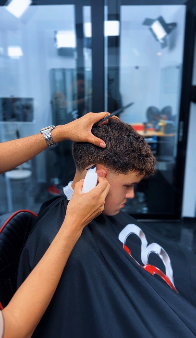 Barber styling young boys hair with hands, applying product in professional salon setting