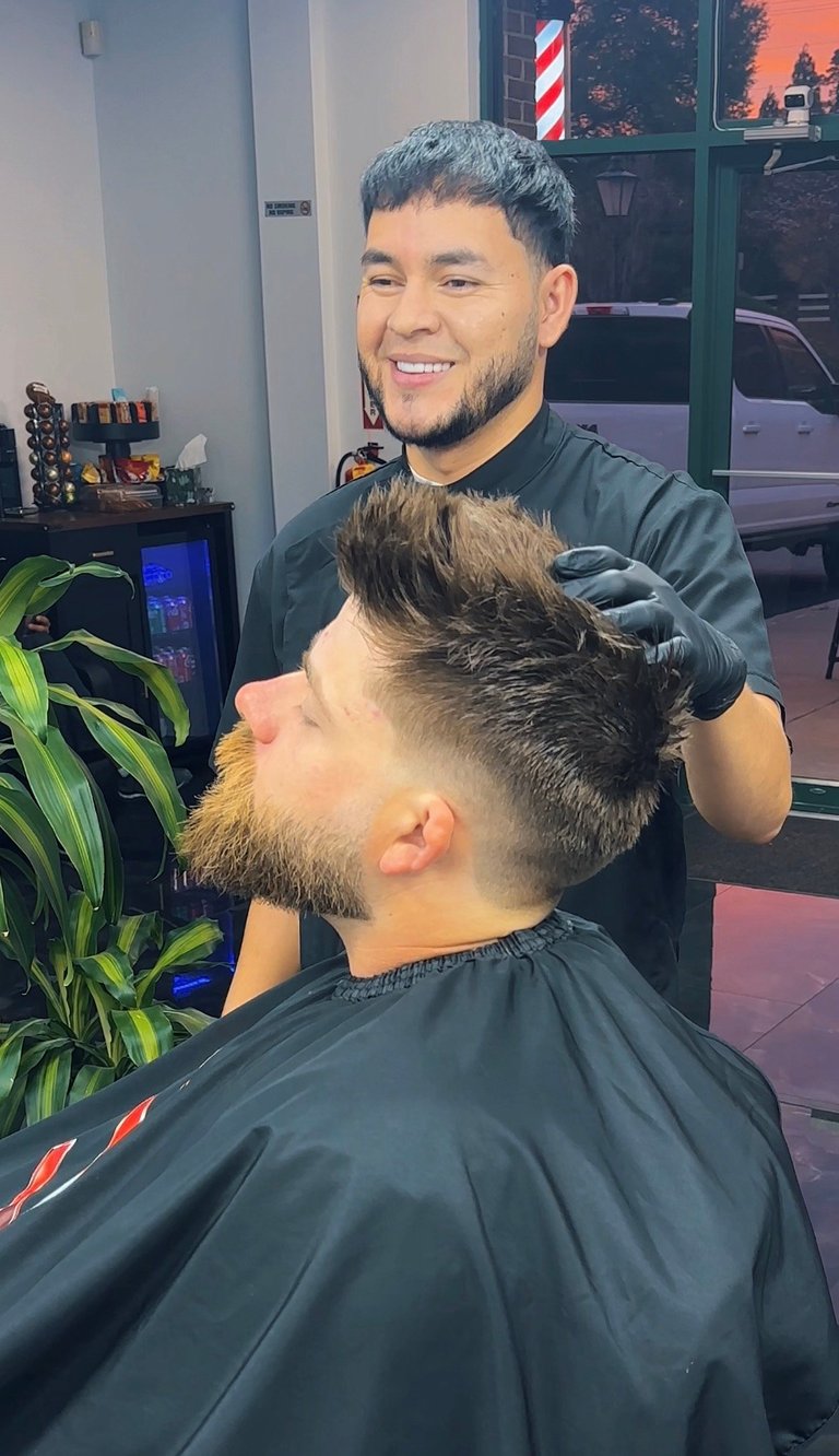 Barber styling a clients hair in a modern barbershop with striped pole visible in background