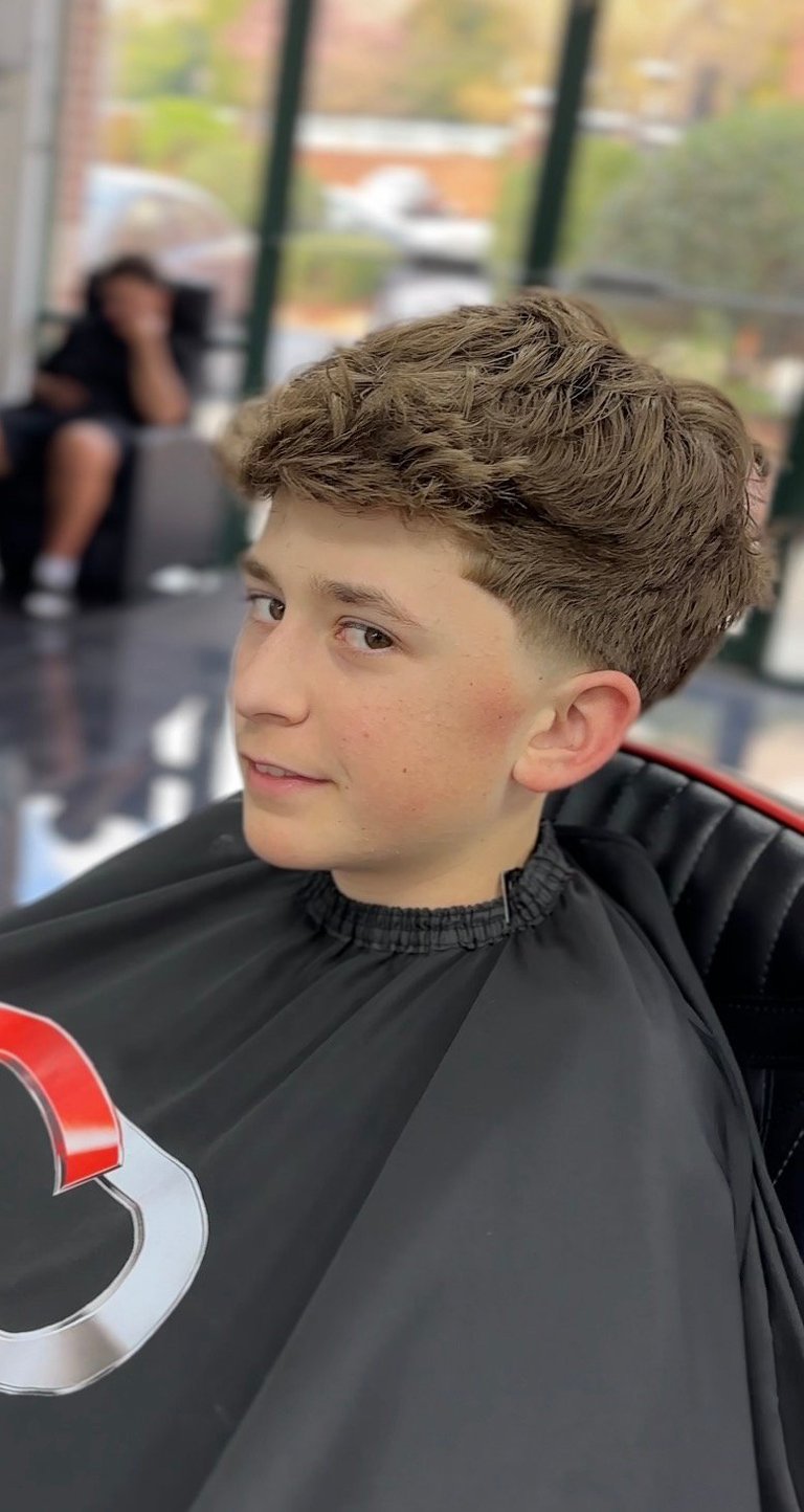 Young boy with a modern textured haircut wearing a black and red barber cape in a salon setting