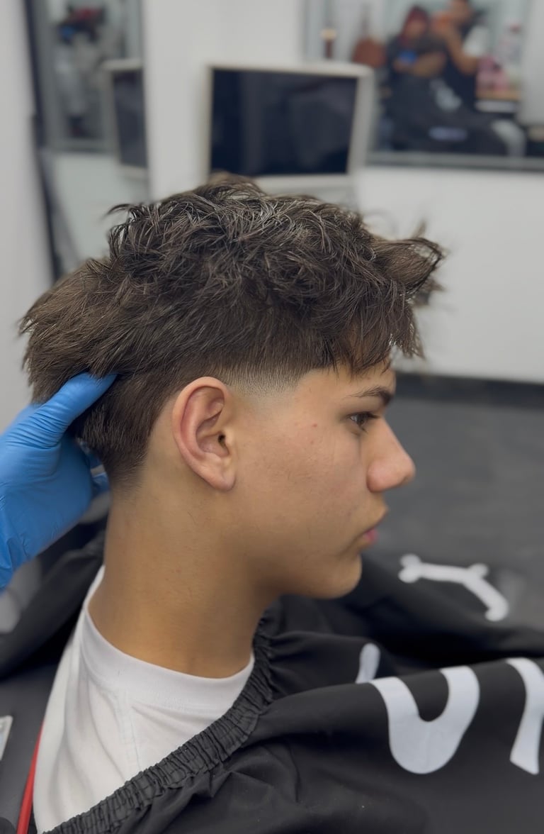 A barber with blue gloves styling a young mans dark textured hair with a fade in a salon setting