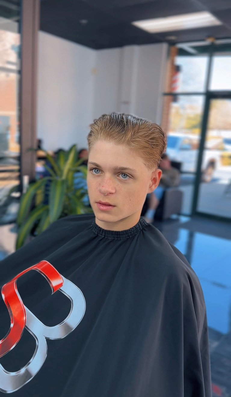 Young person with blonde slicked-back hair in black shirt inside modern gym or fitness facility with blue flooring
